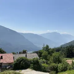 Case con tetti rossi ai piedi del monte Biaina, con valli e montagne azzurre all'orizzonte sotto un cielo limpido.