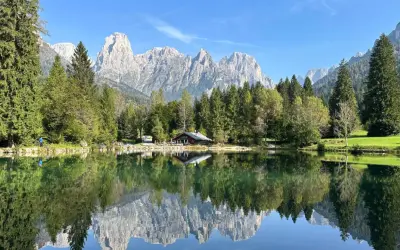 Riflessi perfetti sul lago Welsperg: montagne maestose, boschi verdi e un rifugio alpino.