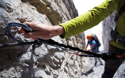 Mano agganciata a cavo d'acciaio su una parete rocciosa, un'avventura tra le ferrate Trentino con un'altra persona sullo sfondo.