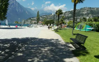 Vacanze in campeggio Europa a Torbole: spiaggia con windsurf, montagne sullo sfondo e area giochi per bambini.
