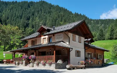 Rifugio Refavaie, un'accogliente struttura alpina con un portico fiorito, immersa nel verde di un bosco di conifere.