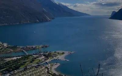 Vista panoramica del lago con montagne sullo sfondo. In primo piano, un lido e un camping vicino ad Arco.