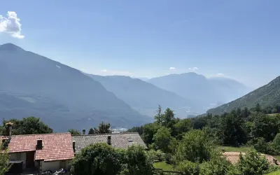 Case con tetti rossi ai piedi del monte Biaina, con valli e montagne azzurre all'orizzonte sotto un cielo limpido.