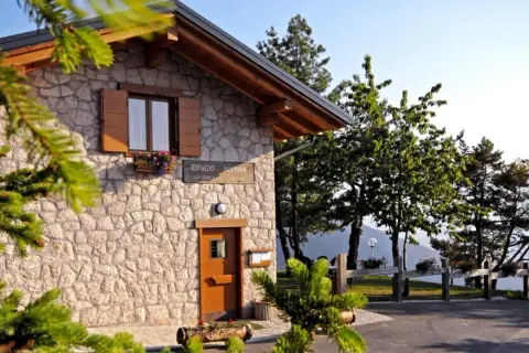Rifugio Predaia, un'accogliente costruzione in pietra con tetto spiovente, circondato da alberi verdi e un cielo azzurro.