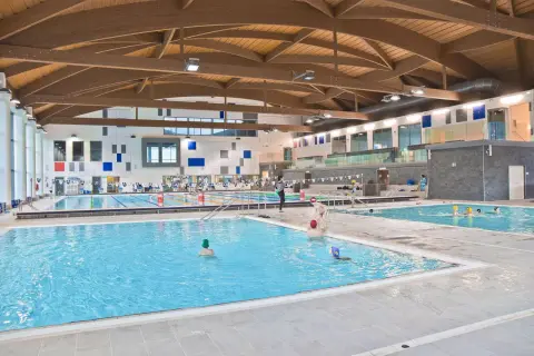Ampia piscina coperta con tetto in legno e diverse corsie. Persone nuotano e si divertono nella piscina Pergine.