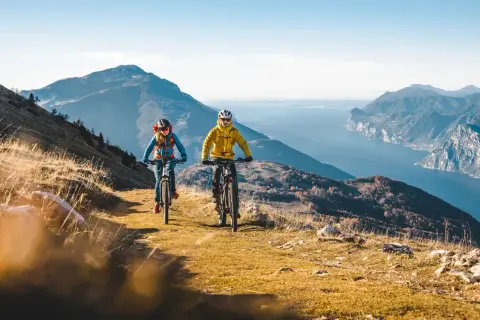 Coppia in mountain bike sui percorsi mtb Trentino, con vista mozzafiato sul lago e le montagne.