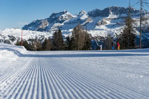 Piste da sci perfettamente battute a Pinzolo, con sciatori sullo sfondo e maestose montagne innevate.