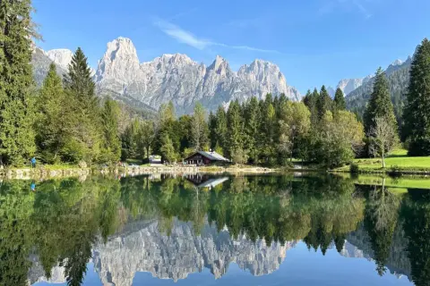 Riflessi perfetti sul lago Welsperg: montagne maestose, boschi verdi e un rifugio alpino.