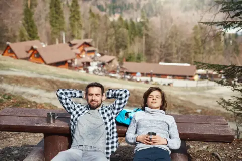 Un padre e un figlio si rilassano su una panchina in montagna, godendosi il sole dopo una passeggiata. Un perfetto weekend in montagna.