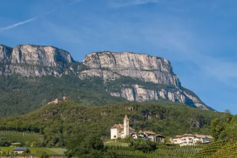 Imponente monte Macaion con vigneti terrazzati e un borgo con chiesa.