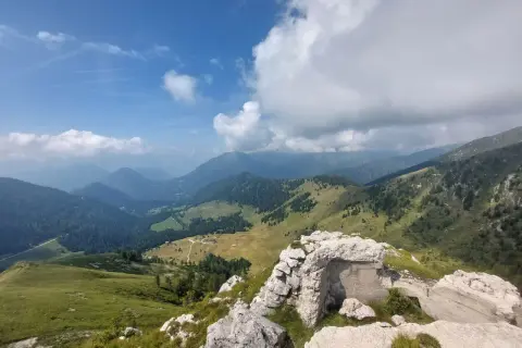 Rovine di un bunker sul **Castello Tesino**, con vista su verdi valli e montagne nebbiose sotto un cielo azzurro e nuvoloso.