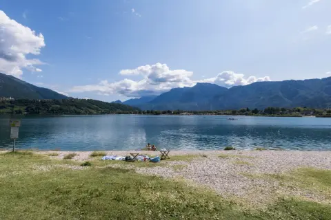 Relaxing day al lido di Caldonazzo, con montagne sullo sfondo e persone che si godono il sole e il lago.