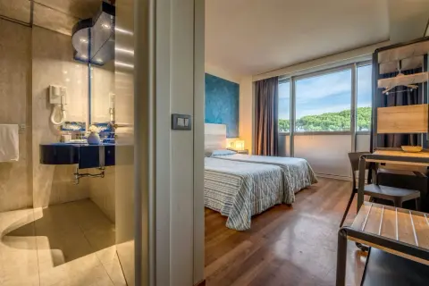 Camera d'albergo con due letti, bagno blu e vista sul verde. Ideale per sapere dove dormire a Pisa.