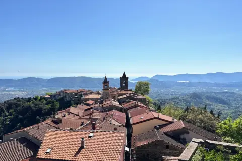 Panoramica di un borgo collinare con tetti rossi e campanili, che rivela dove si trova Fosdinovo, con il mare e le montagne all'orizzonte.