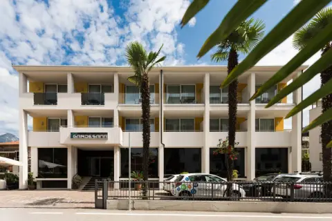 Hotel Gardesana a Riva del Garda, con palme e cielo azzurro. Un'auto bianca parcheggiata davanti.