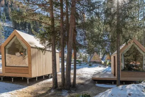 Piccole case in legno con grandi vetrate, immerse in un bosco innevato. Un'oasi di pace per alloggi particolari.