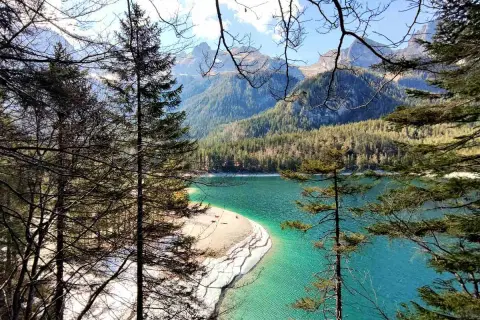 Un lago turchese incorniciato da alberi e montagne nel Val di Non. La spiaggia sabbiosa invita a una sosta.