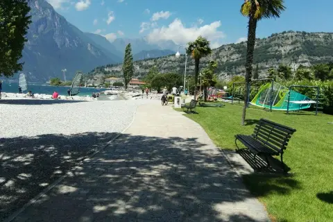 Vacanze in campeggio Europa a Torbole: spiaggia con windsurf, montagne sullo sfondo e area giochi per bambini.