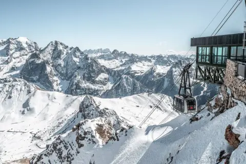 Panoramica mozzafiato dal belvedere di Canazei: una funivia scende tra le cime innevate delle Dolomiti.