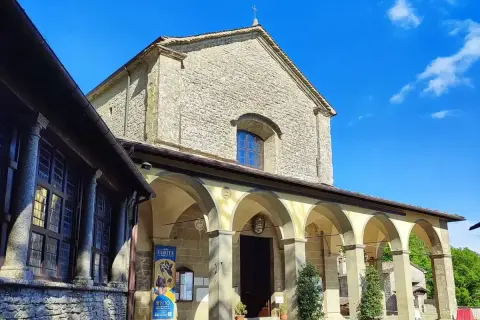La Verna, luogo sacro con un portico ad archi che conduce all'ingresso di una chiesa in pietra, sotto un cielo azzurro.
