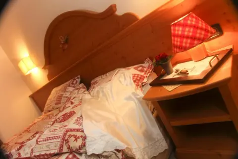 Camera accogliente all'hotel La Romantica Moena, con letto decorato e comodino con fiori.