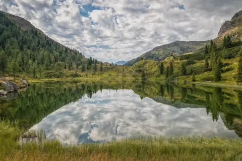 Lago alpino con riflessi di montagne e cielo nuvoloso, un'oasi di pace in una splendida cavalese estate.