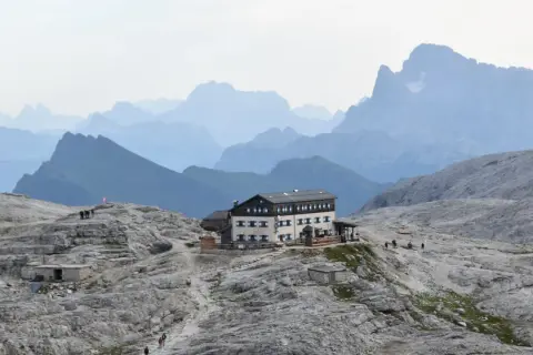 Il rifugio Rosetta, un edificio imponente, si erge su un terreno roccioso con montagne sfumate all'orizzonte.