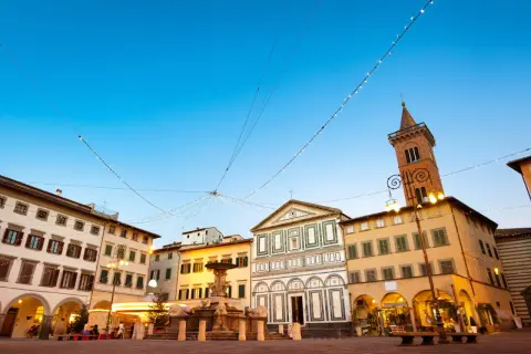 Piazza di Empoli illuminata da luci natalizie, con la fontana, la chiesa e il campanile che si stagliano sotto un cielo azzurro.