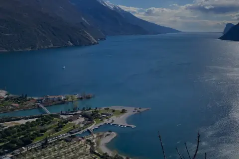 Vista panoramica del lago con montagne sullo sfondo. In primo piano, un lido e un camping vicino ad Arco.