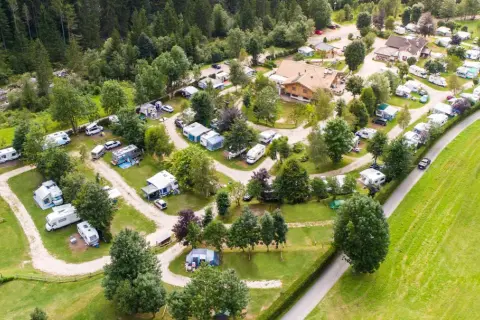 Vista aerea di un campeggio immerso nel verde, con roulotte, camper e tende disposti su prati e sentieri. Un luogo ideale per una vacanza in **camping valle verde**.