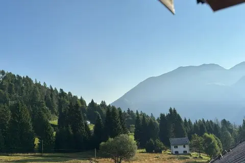 Un casolare bianco, forse la locanda La Ruscoletta, immerso nel verde di un prato e circondato da alberi, con montagne nebbiose sullo sfondo.