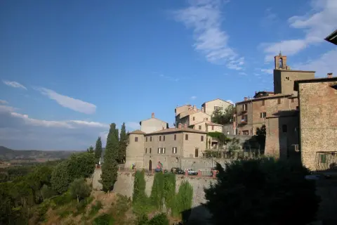 Borgo medievale di Panicale, Perugia, con case in pietra e mattoni, cipressi e vista sulla campagna umbra sotto un cielo azzurro.
