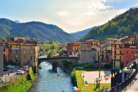 Borgo pittoresco in Garfagnana, cosa vedere: un fiume serpeggia tra case colorate e colline verdi, con un antico ponte in pietra.