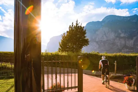 Ciclista in sella alla bici, con montagne sullo sfondo. Un raggio di sole illumina la scena vicino al bicigrill Faedo.