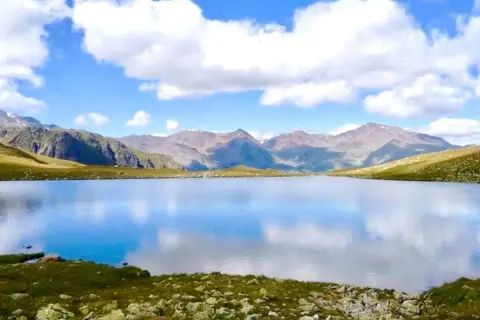 Un sereno lago alpino riflette il cielo azzurro e le montagne. Un paesaggio da sogno nel Trentino.