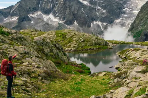 Due escursionisti ammirano un lago alpino e montagne imponenti, seguendo il sentiero della pace.