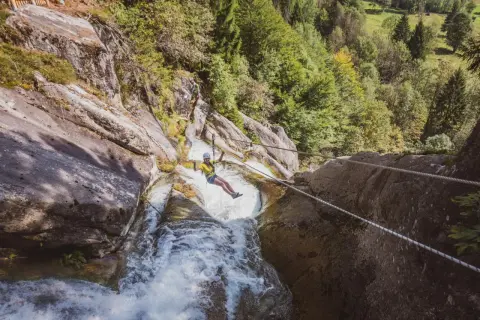 Donna in zipline sopra una cascata nella Val Daone, con rocce e alberi circostanti.