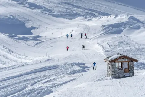 Sciare su piste battute, un piccolo rifugio in pietra e sciatori che godono della loro settimana bianca.