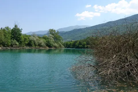 Acque turchesi del lago di Cavedine circondato da rigogliosa vegetazione e montagne sullo sfondo.