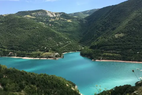 Splendido lago di Fiastra con acque turchesi, incastonato tra verdi colline boscose sotto un cielo azzurro.