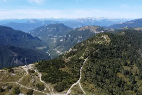 Sentiero che sale verso la croce sul monte Maggio, con vista su valli verdi e montagne all'orizzonte.