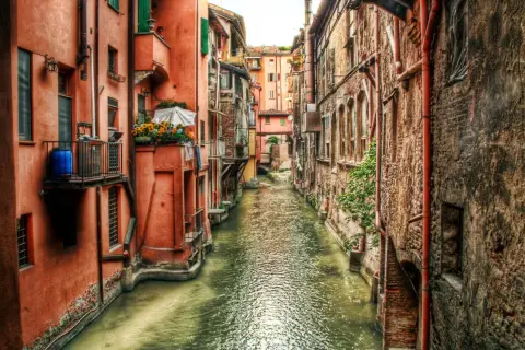 Un canale con edifici color ocra e mattoni, un assaggio di cosa vedere a Bologna, con fiori su un balcone.