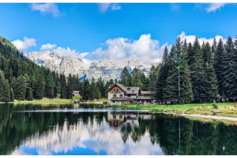 Riflessi sull'acqua del lago Nambino, con un rifugio alpino e montagne sullo sfondo.