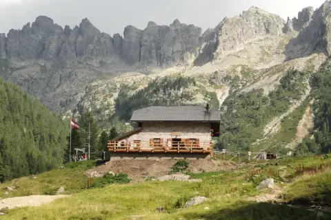 Il rifugio Caldenave, un'accogliente baita in pietra, si erge su un prato verde ai piedi di imponenti montagne rocciose.