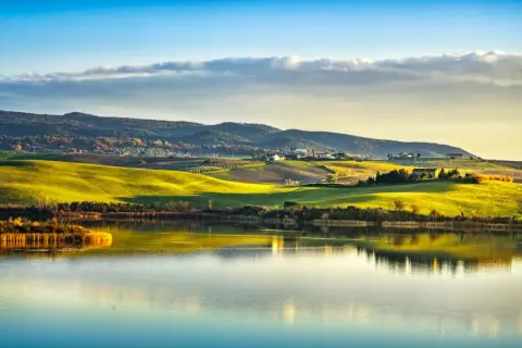 Dolci colline toscane illuminate dal sole al tramonto si specchiano nel lago di Santa Luce, creando un paesaggio incantevole.