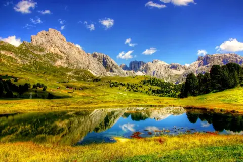 Un lago alpino riflette montagne maestose e prati verdi. Perfetto per le cose da fare in estate: escursioni, relax e ammirare la natura.