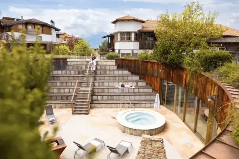 Relaxing at Pineta Nature Resort: un uomo prende il sole su una scalinata in legno, vicino a una vasca idromassaggio e a un edificio moderno.