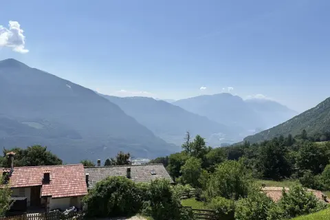 Case con tetti rossi ai piedi del monte Biaina, con valli e montagne azzurre all'orizzonte sotto un cielo limpido.