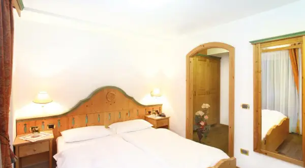Camera accogliente con letto matrimoniale, arredi in legno e un'apertura verso un armadio. Il tuo soggiorno al hotel Diamant Park sarà rilassante.
