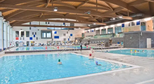 Ampia piscina coperta con tetto in legno e diverse corsie. Persone nuotano e si divertono nella piscina Pergine.